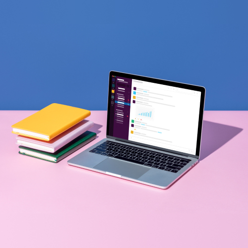 Une pile de livres placée à côté d’un ordinateur portable sur lequel l’application Slack est ouverte.